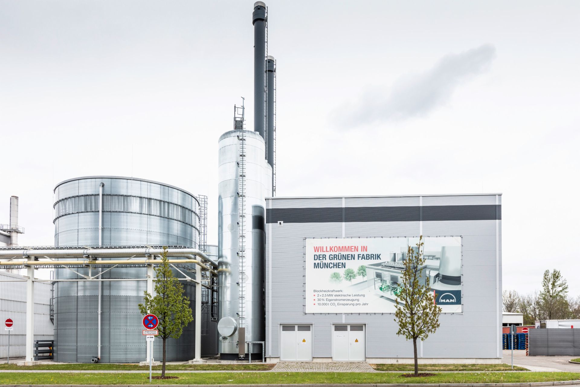 Außenansicht der Grünen Fabrik München mit Industriegebäuden und einem Schild, das die umweltfreundlichen Initiativen hervorhebt.