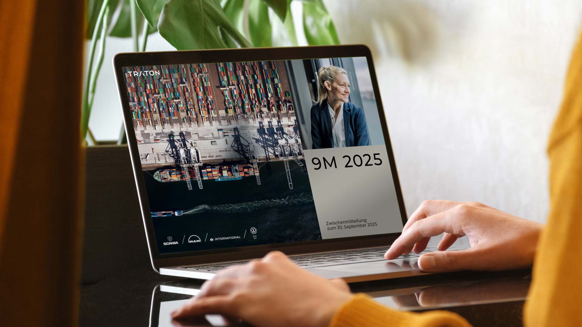 Eine Person in einem gelben Pullover benutzt einen Laptop auf einem dunklen Tisch. Auf dem Bildschirm ist eine Geschäftspräsentation mit dem Titel „9M 2025 – Zwischenmitteilung zum 30. September 2025“ der TRATON Group zu sehen. Der Bildschirm zeigt ein Containerschiff aus der Vogelperspektive, ein Porträt einer lächelnden Geschäftsfrau und die Logos der TRATON-Marken, darunter Scania, MAN, International und Volkswagen Truck & Bus.