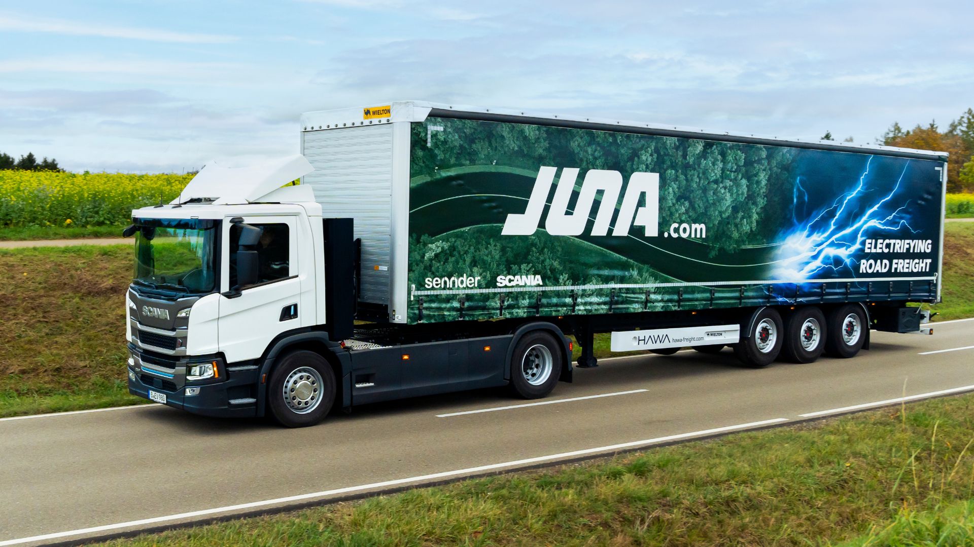 Ein elektrischer Scania-Lkw fährt durch eine ländliche Landschaft und ist Teil von JUNA, dem Joint Venture von Scania und sennder.