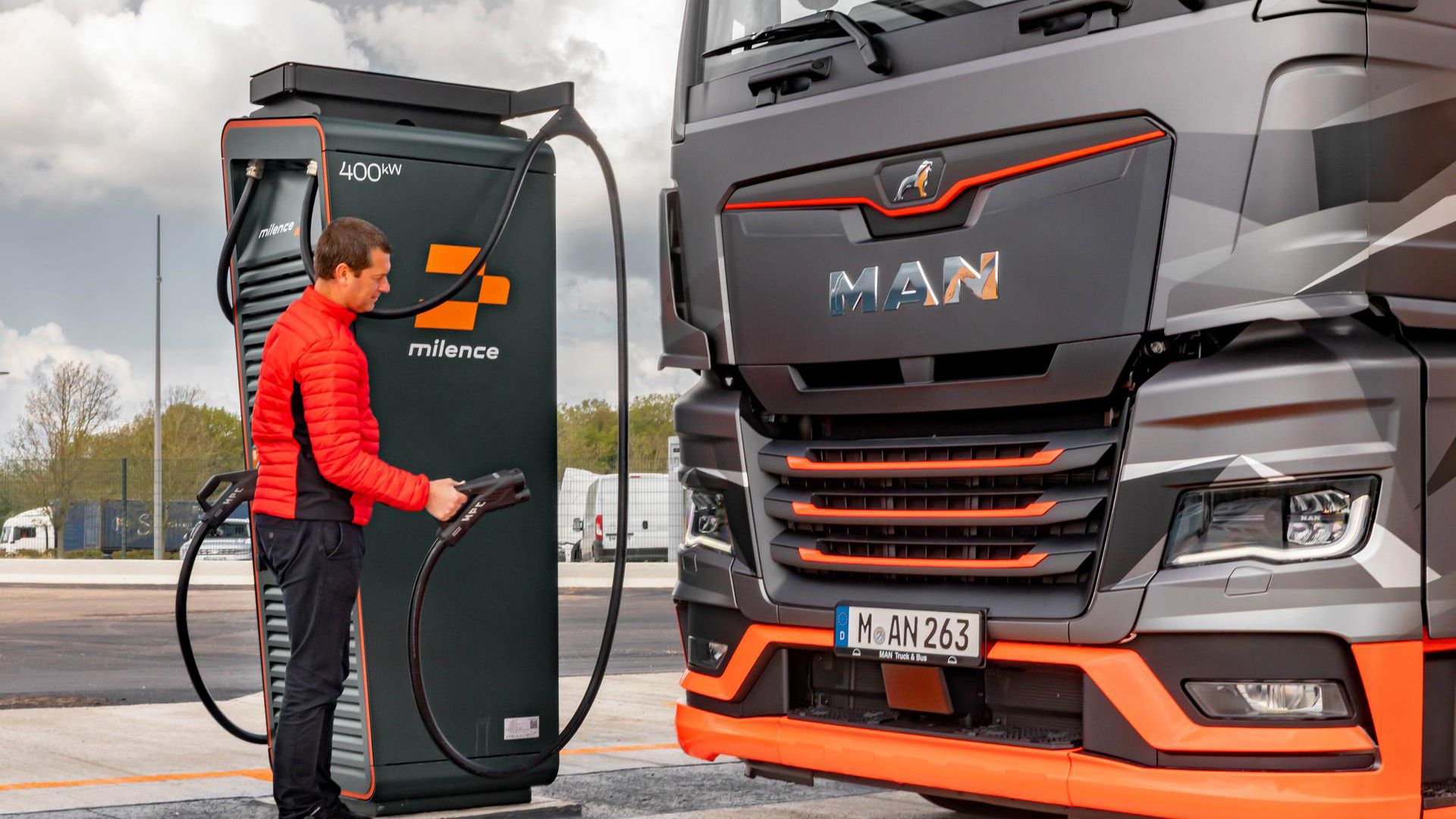 Ein MAN-LKW wird an einer Milence-Ladestation geladen, wobei eine Person das Ladekabel bedient. 