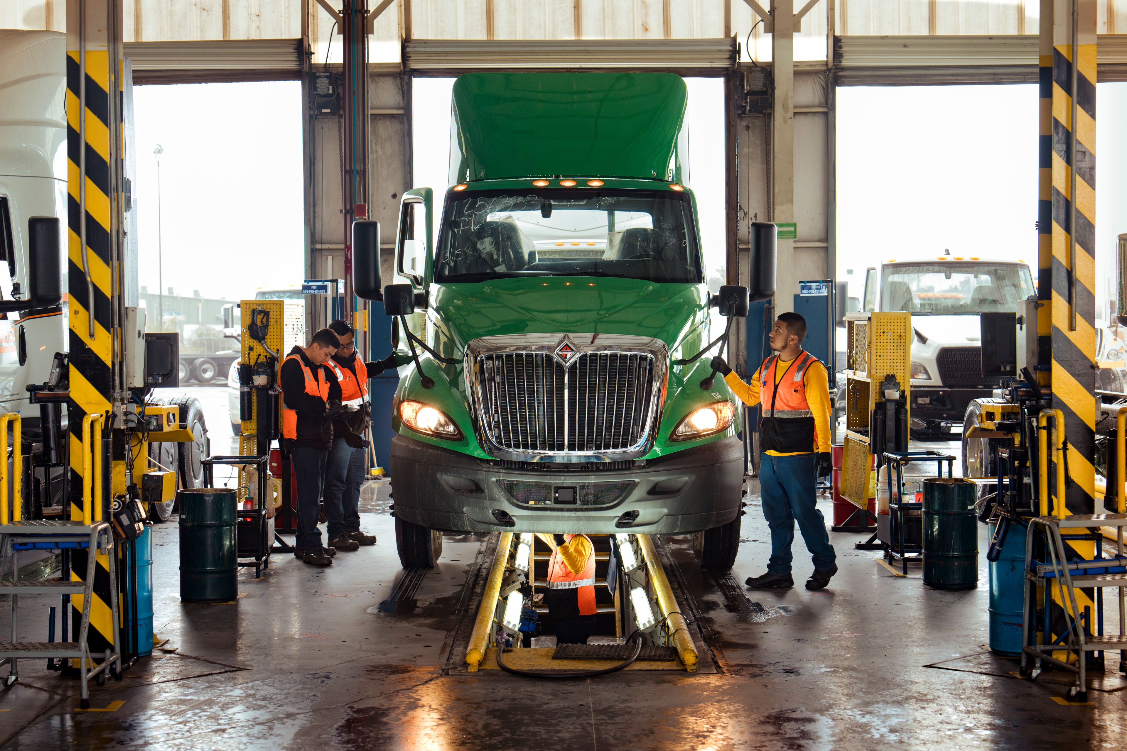 International employees wearing security vests surrounding a green International truck and working underneath it. 