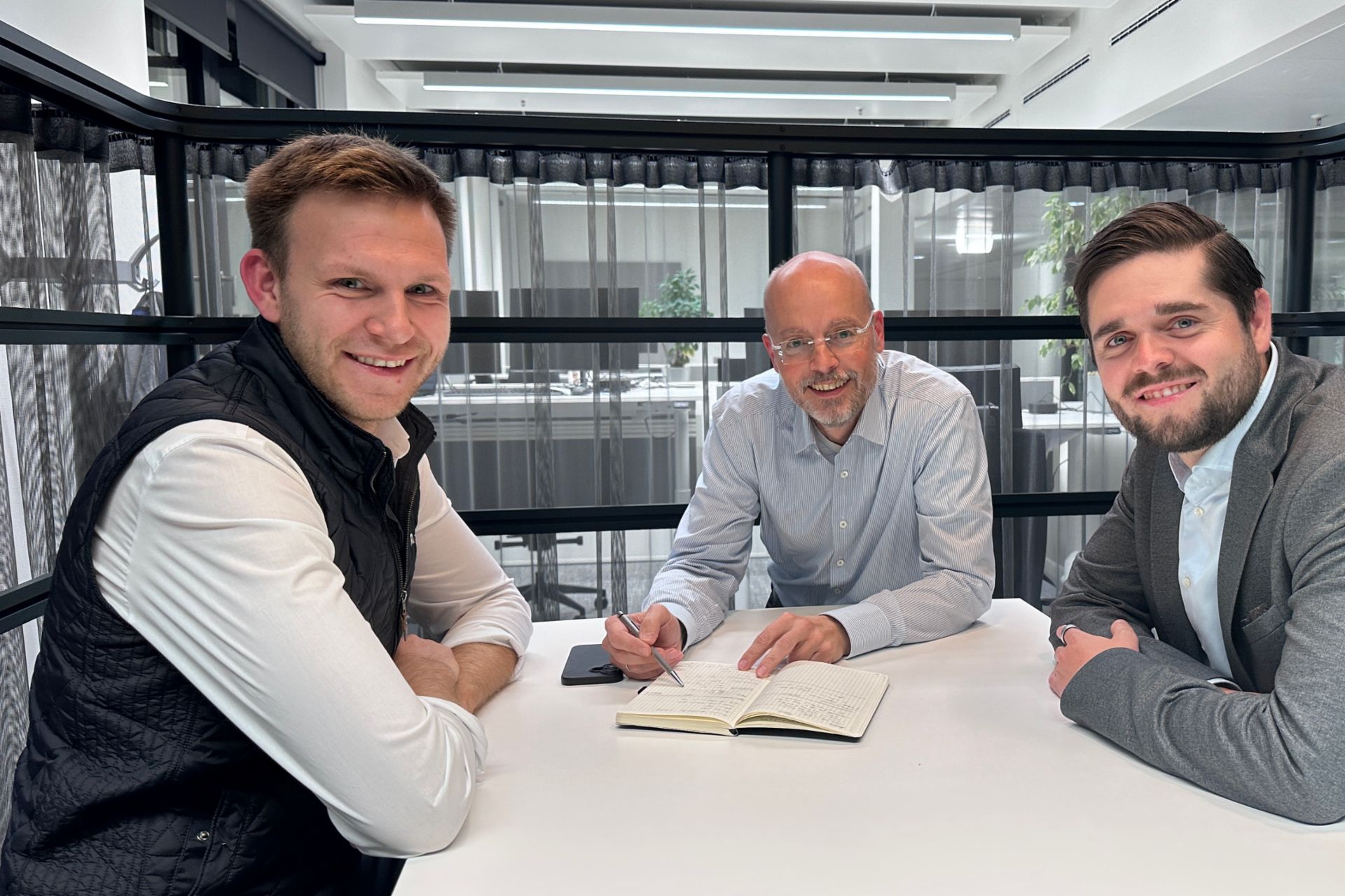 Drei Männer sitzen an einem Tisch und lächeln. 