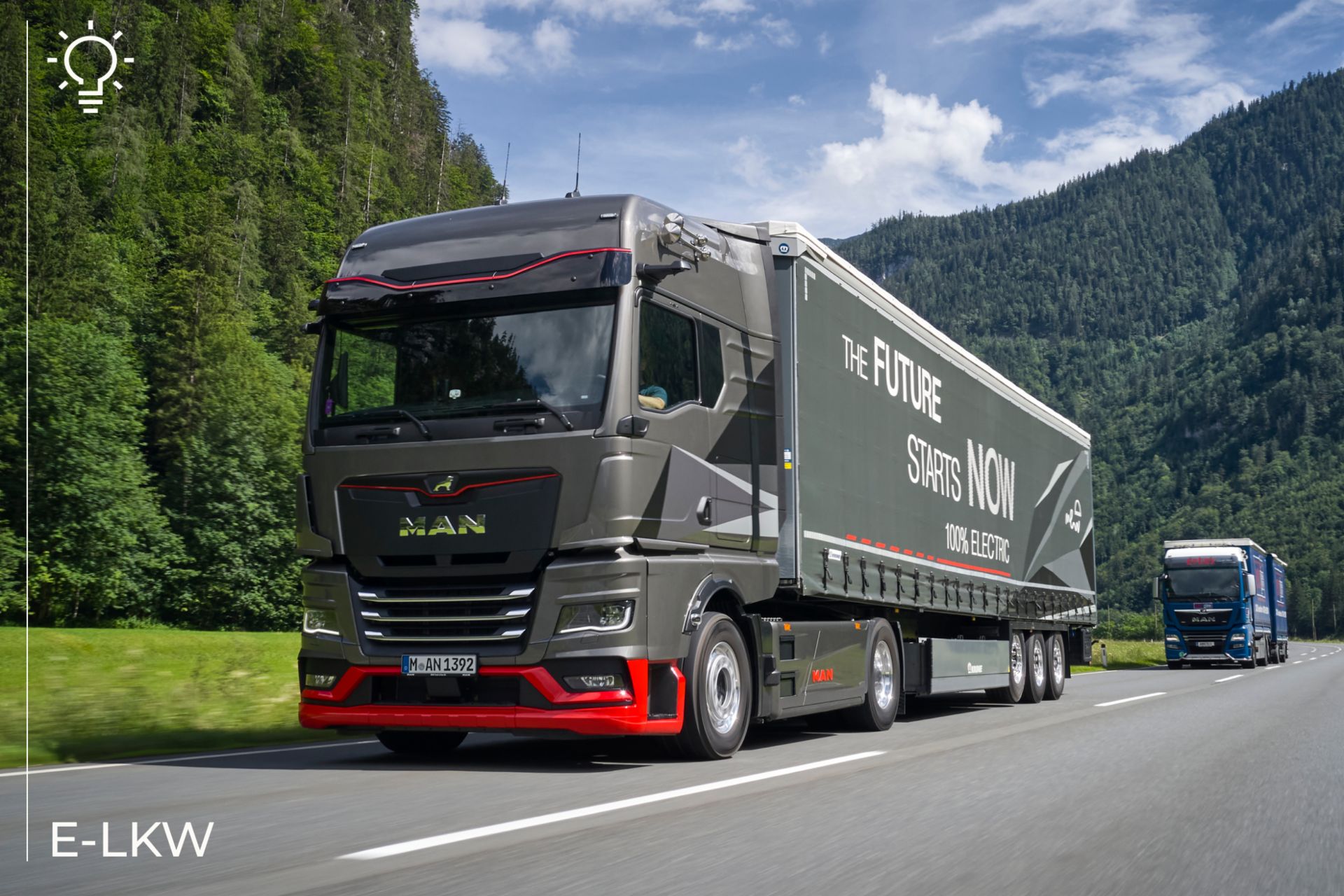 Ein Foto eines modernen elektrischen MAN-Lkw, der auf einer Autobahn durch ein bergiges und bewaldetes Gebiet fährt. Der Anhänger des Lkw zeigt die Botschaft 
