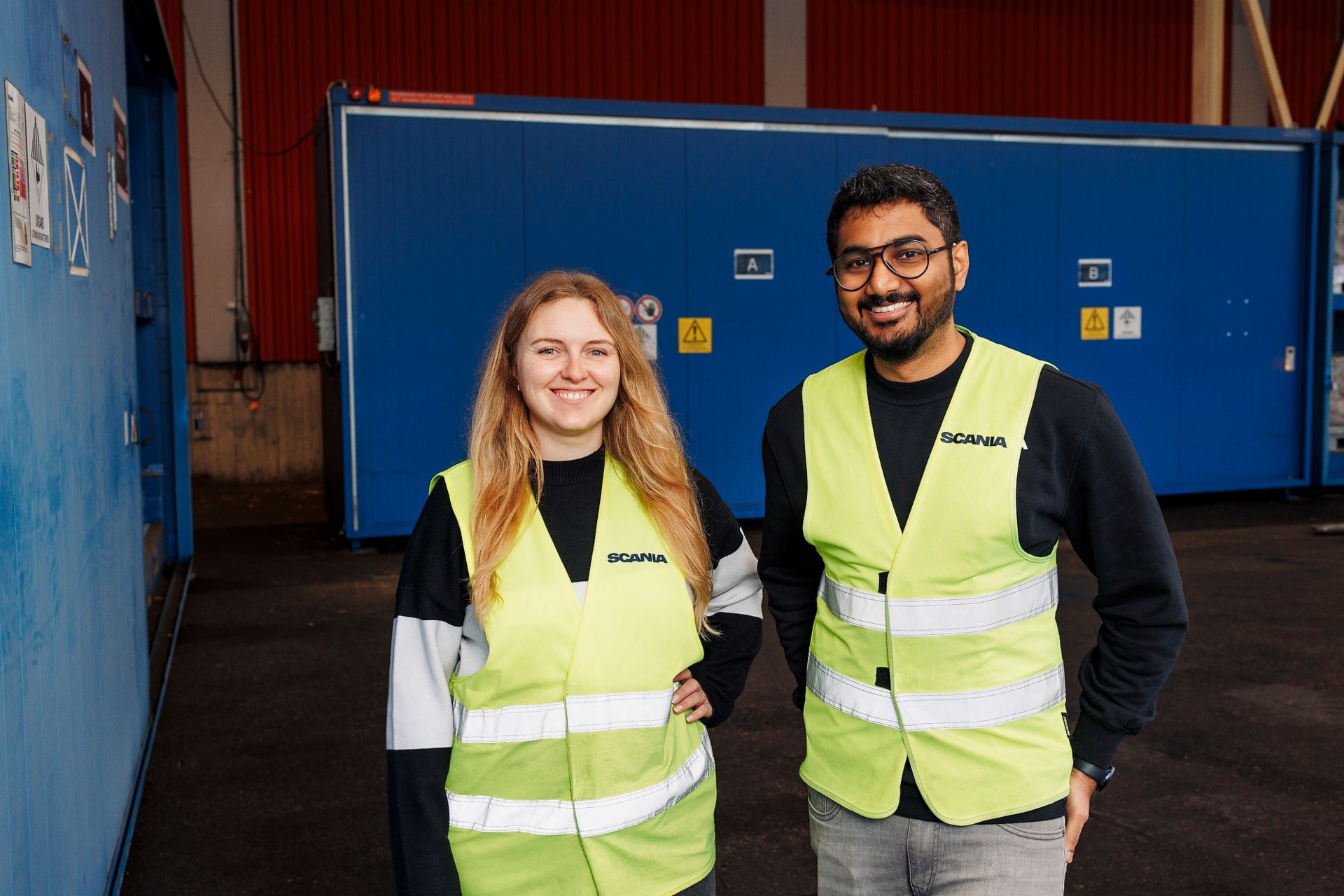 Battery production engineers Christina Brunhardt (MAN) and Aswin Ravikumar (Scania) are wearing yellow security vests at a battery warehouse. They are part of the team developing production solutions for future battery platforms. 