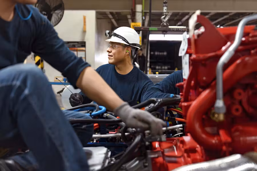 Technician in uniform working on a diesel engine in a clean industrial setting.
